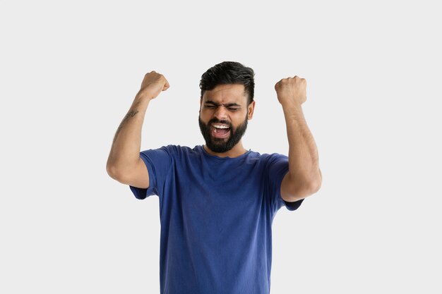 Schönes männliches Porträt lokalisiert. Junger emotionaler hinduistischer Mann im blauen Hemd. Gesichtsausdruck, menschliche Emotionen. Feiern wie ein Gewinner.