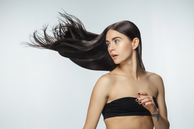 Schönes Modell mit langen glatten, fliegenden brünetten Haaren lokalisiert auf weißem Studiohintergrund.