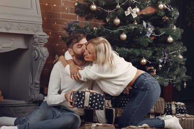 Schönes Paar, das zu Hause nahe Weihnachtsbaum sitzt