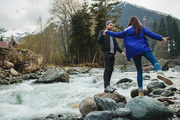 Schönes Paar des jungen Hipsters in der Liebe, die auf einem Felsen am Fluss im Winterwald geht