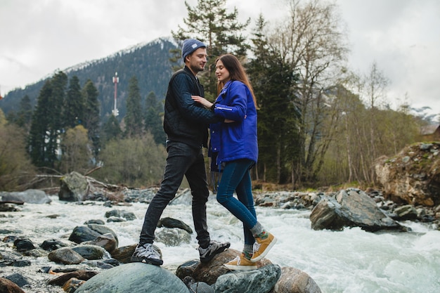 Schönes Paar des jungen Hipsters in der Liebe, die auf einem Felsen am Fluss im Winterwald geht