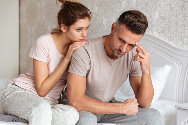 Schönes Paar sitzt auf dem Bett, während die Frau ihren Freund beruhigt, der verärgert ist.