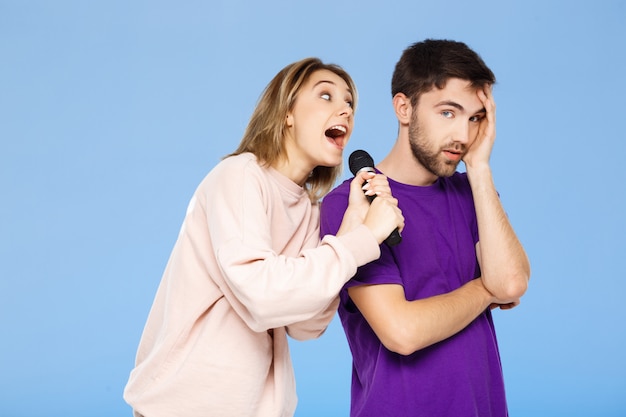 Schönes Paar über blauer Wand. Mädchen, das im Mikrofonmann singt, erfreute sich.