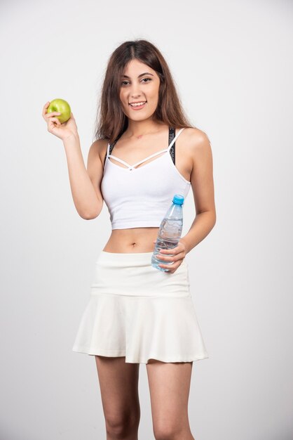 Schönes Porträt der jungen Frau mit einem grünen Apfel und einer Flasche Wasser.