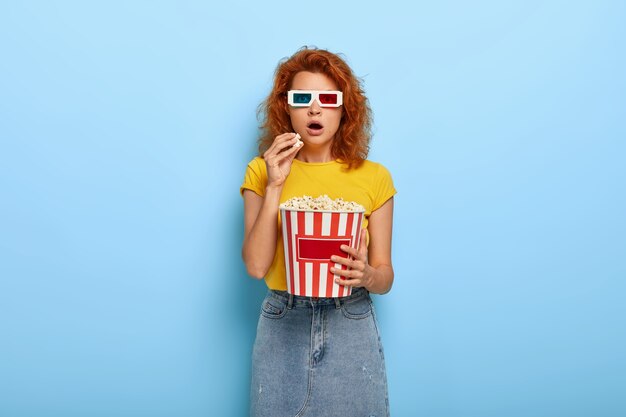 Schönes schockiertes Ingwer charmantes Mädchen hält Eimer mit Popcorn