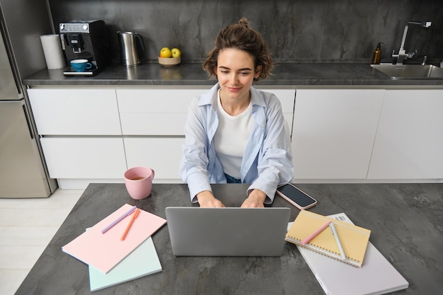 Schönes selbständiges Mädchen arbeitet von zu Hause aus, junge Frau studiert online, schaut Kurs auf der Website, schaut auf den Laptop-Bildschirm