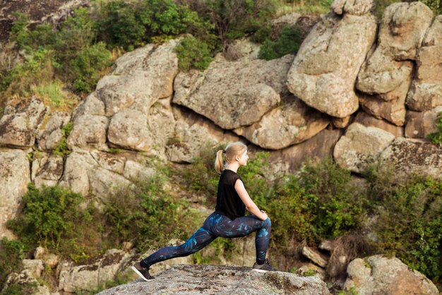 Schönes sportliches blondes Frauentraining, das sich auf Felsen im Canyon ausdehnt