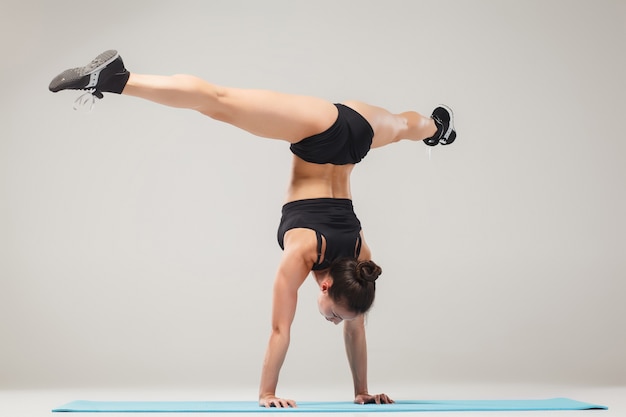 Schönes sportliches Mädchen, das in der Akrobatenhaltung oder in der Yoga-Asana auf grauem Hintergrund steht