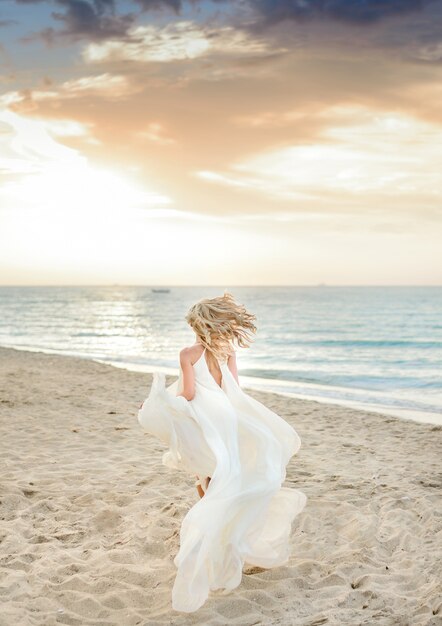 Schönes stilvolles Mädchen, das im Sonnenlicht auf dem Strand aufwirft