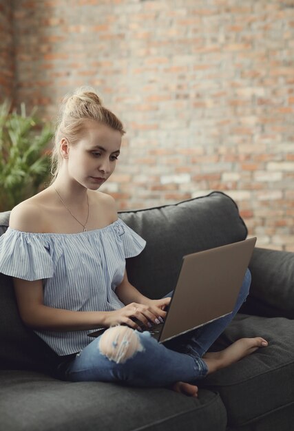 Schönes Teenager-Mädchen mit Laptop, im Sofa sitzend