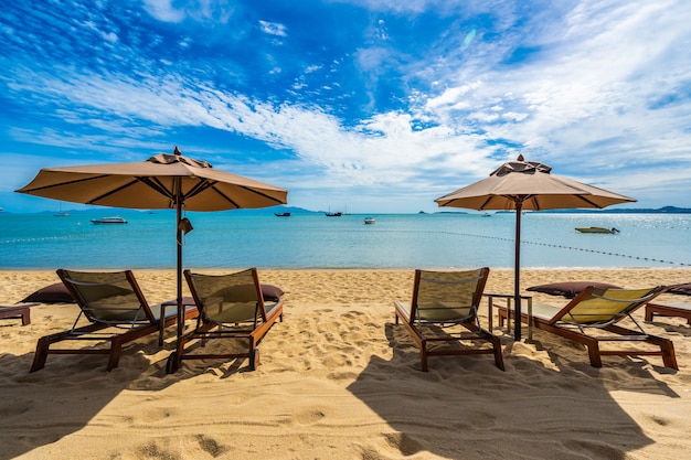 Schönes tropisches Strandmeer und -ozean mit KokosnussPalme und Regenschirm und Stuhl auf blauem Himmel