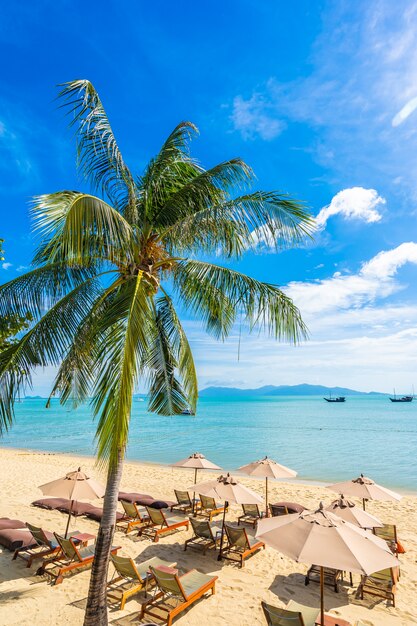 Schönes tropisches Strandmeer und -ozean mit KokosnussPalme und Regenschirm und Stuhl auf blauem Himmel