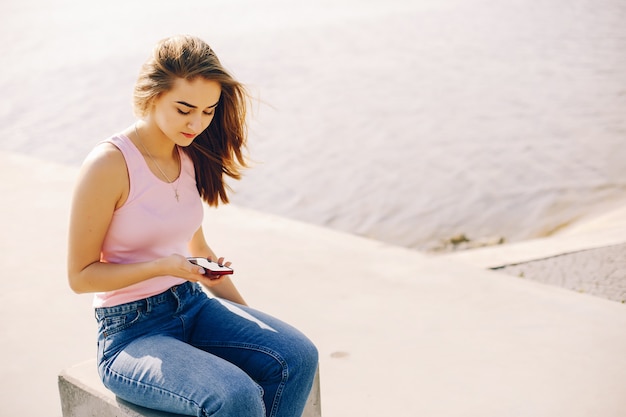 schönes und helles Mädchen im rosa T-Shirt und in den Blue Jeans, die im sonnigen Sommerpark sitzen