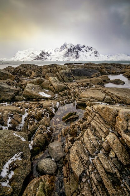 Schönes vertikales Bild eines felsigen Atlantikufers mit schneebedecktem Berg