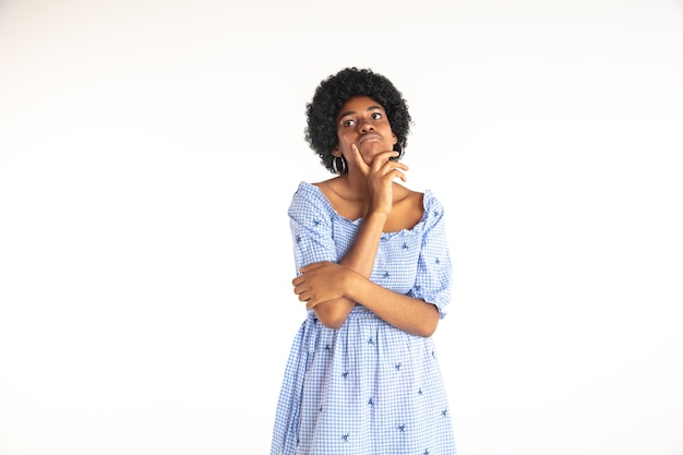 Schönes weibliches Brustbild auf weißem Studiohintergrund. Junge emotionale Afroamerikanerfrau im blauen Kleid.