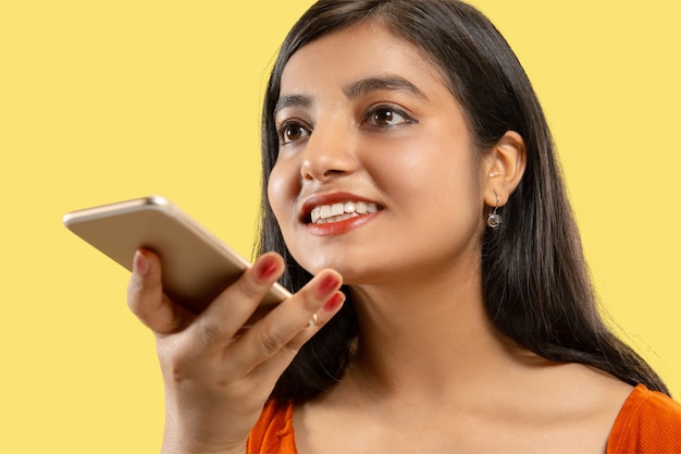 Schönes weibliches halbes Längenporträt lokalisiert. Junge emotionale indische Frau im Kleid, das am Telefon spricht. Negativer Raum. Gesichtsausdruck, menschliches Gefühlskonzept.