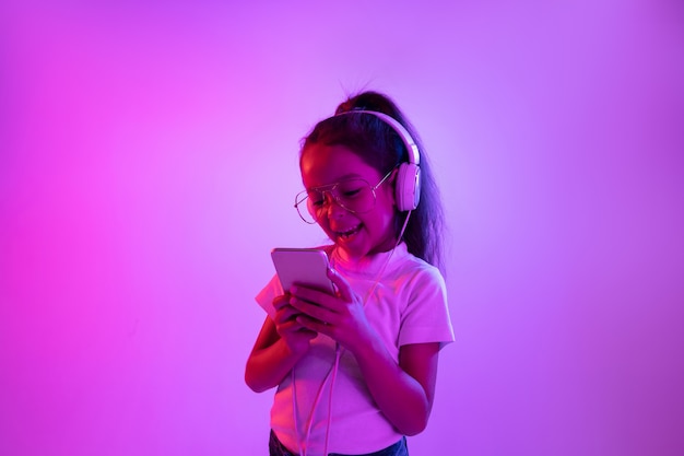 Schönes weibliches halblanges Porträt lokalisiert auf lila Hintergrund im Neonlicht. Emotionales Mädchen in der Brille. Menschliche Emotionen, Gesichtsausdruckkonzept. Musik hören, Selfie machen, spielen.