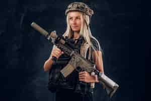 Kostenloses Foto schönes zerbrechliches blondes mädchen mit maschinengewehr in voller armeeuniform und helm.