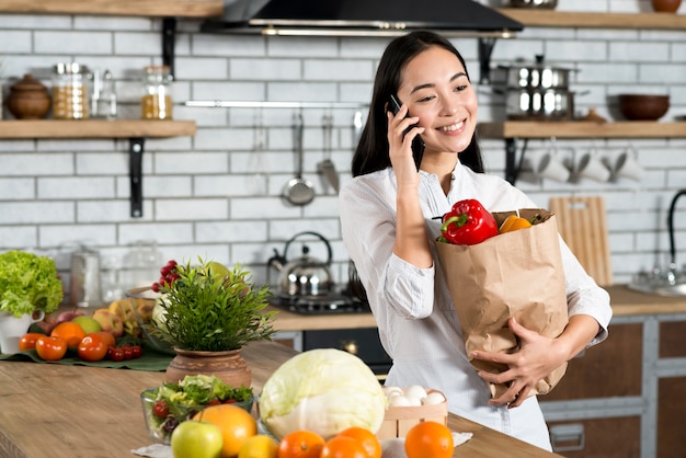 Schönheit, die auf dem Mobiltelefon hält braune Gemüsetasche spricht