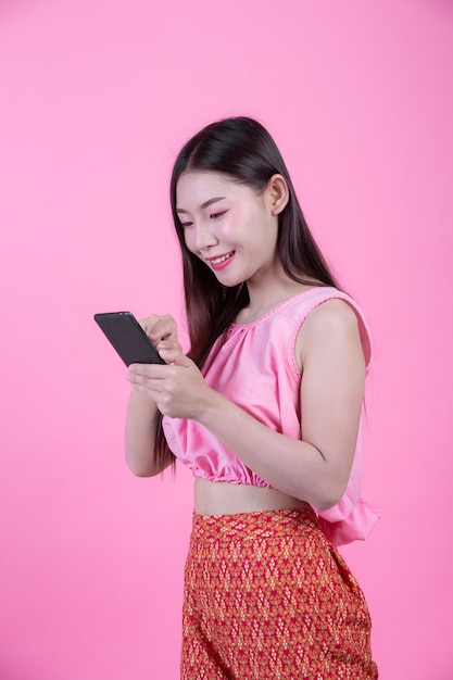 Schönheit, die einen Smartphone auf einem rosa Hintergrund hält.