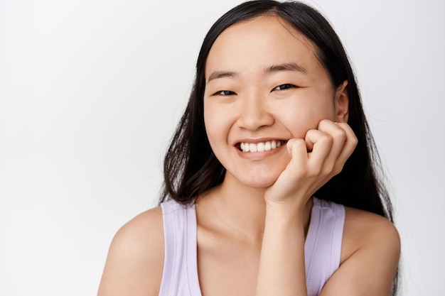 Schönheit Junge asiatische Frau mit glühender gesunder Haut und weißen Zähnen, die Hautpflegeprodukt oder Kosmetik annonciert, die gegen weißen Hintergrund stehen