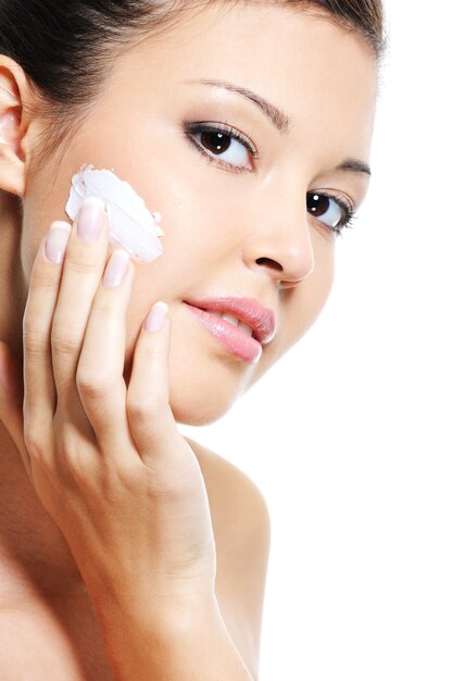 Schönheit kaukasische weibliche Hautpflege ihres Gesichts durch Auftragen von kosmetischer Feuchtigkeitscreme auf ihre Wange