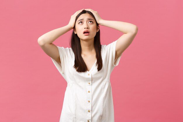 Schönheit, Menschengefühle und Sommerfreizeitkonzept. Verzweifelte und frustrierte junge asiatische frau in panik, blick auf den himmel liebe gott hilfe, greife den alarmierten kopf, stehend ängstlich rosa hintergrund.