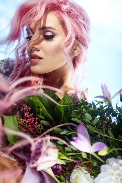 Schönheit mit dem rosa Haar hält großen Blumenstrauß mit dem Grün und den violetten Blumen
