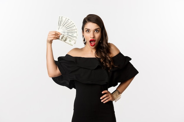 Schönheits- und Einkaufskonzept. Modische Frau mit roten Lippen, Dollar zeigend und lächelnd, über weißem Hintergrund mit Geld stehend.
