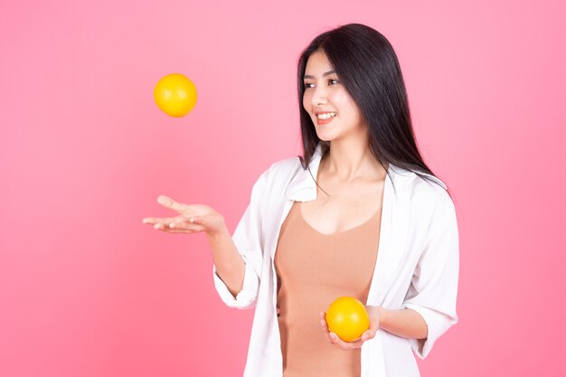 Schönheitsfrau Asiatisches nettes Mädchen fühlen sich glücklich holdind orange Frucht für gute Gesundheit auf rosa Hintergrund