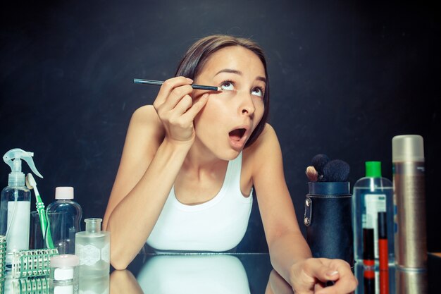 Schönheitsfrau, die Make-up anwendet. Schönes Mädchen, das in den Spiegel schaut und Kosmetik mit einem Eyeliner anwendet.