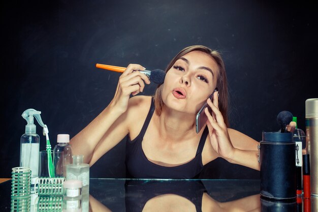 Schönheitsfrau, die Make-up anwendet. Schönes Mädchen, das in den Spiegel schaut und Kosmetik mit einem großen Pinsel anwendet. Kaukasisches Modell im Studio