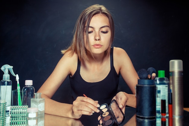 Schönheitsfrau, die Make-up anwendet. Schönes Mädchen, das in den Spiegel schaut und Kosmetik mit einem Pinsel anwendet. Kaukasisches Modell im Studio