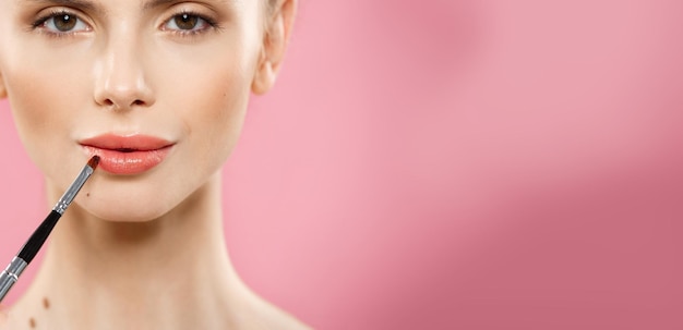 Schönheitskonzept Frau, die roten Lippenstift mit rosa Studiohintergrund aufträgt Schönes Mädchen macht Make-up