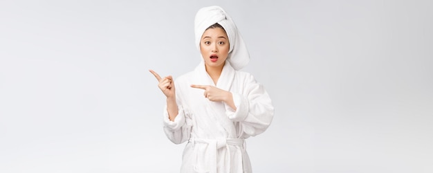 Schönheitsporträt der jungen frau, die finger auf leeren kopienraum zeigt und zeigt asiatische schönheit im bademantel