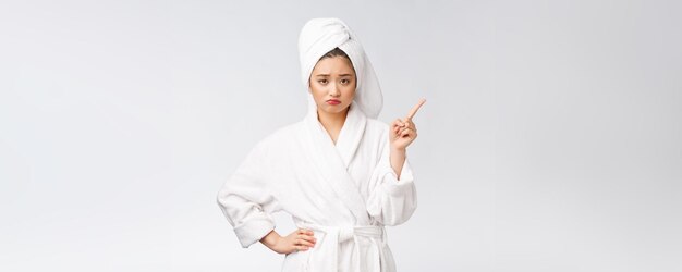 Schönheitsporträt der jungen frau, die finger auf leeren kopienraum zeigt und zeigt asiatische schönheit im bademantel