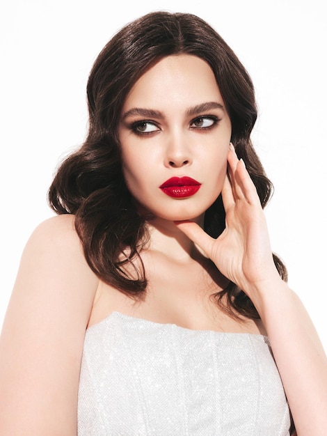 Schönheitsporträt einer jungen brünetten Frau mit abendlichem Make-up und perfekt sauberer Haut Sexy Modell mit lockigem Haar posiert im Studio mit roten hellen natürlichen Lippen in silbernem Kleid