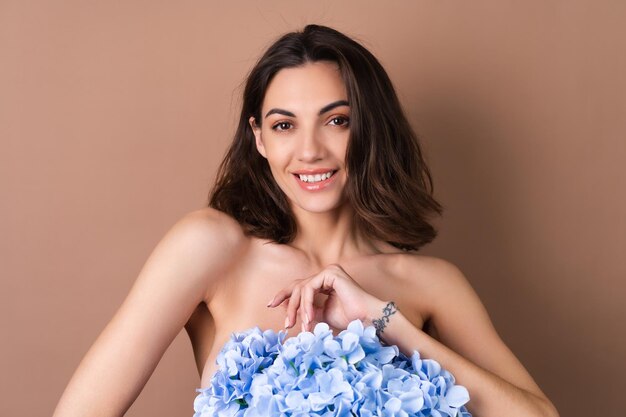 Schönheitsporträt einer toplessen Frau mit perfekter Haut und natürlichem Make-up auf beigem Hintergrund, die einen Strauß bunter Blumen hält