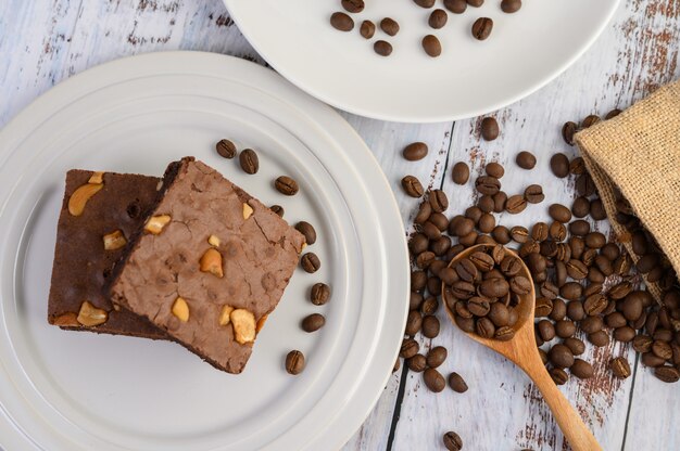 Schokoladen-Brownies auf einem weißen Teller und Kaffeebohnen auf einem Holzlöffel.