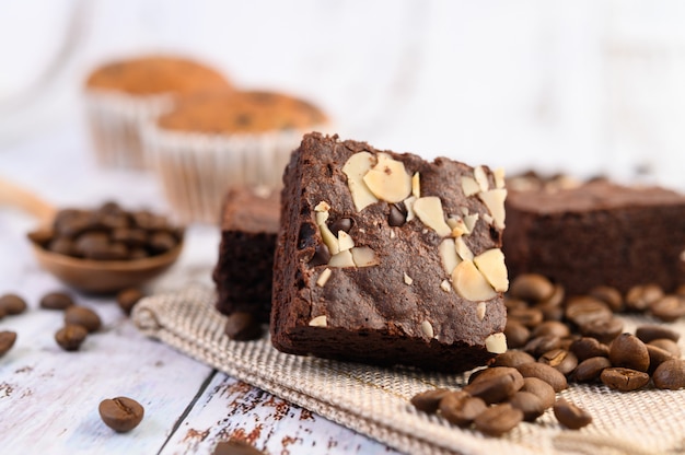 Schokoladen-Brownies auf Sackleinen und Kaffeebohnen auf einem Holztisch.