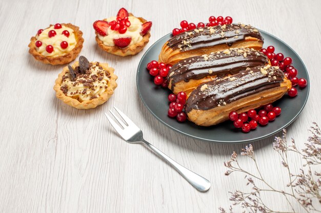 Schokoladen-Eclairs und Johannisbeeren von unten auf den grauen Tellerplätzchen eine Gabel auf dem weißen Holztisch