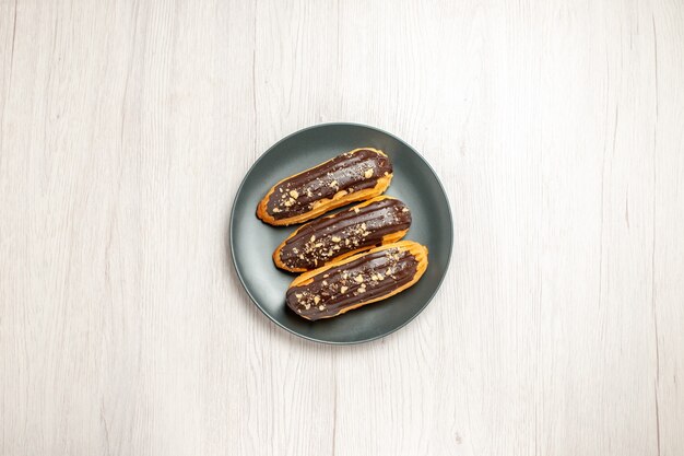 Schokoladen-Eclairs von oben auf dem grauen Teller in der Mitte des weißen Holzbodens