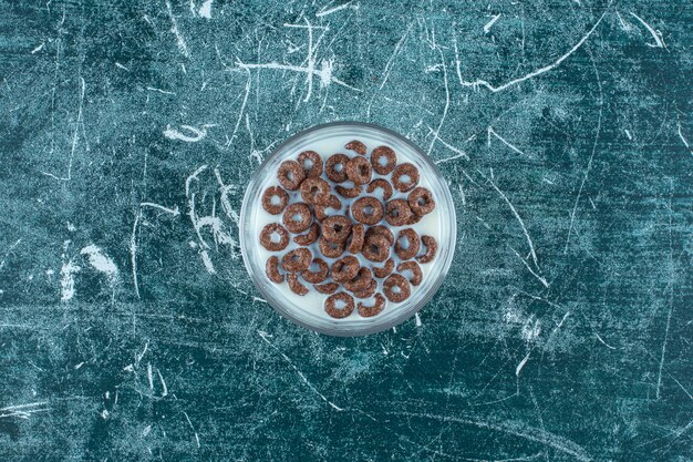 Schokoladen-Getreideflocken-Ringe mit Milch in einer Glasschüssel, auf blauem Hintergrund. Foto in hoher Qualität