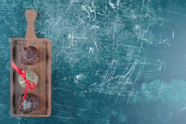 Schokoladencupcakes und ein mit Süßigkeiten überzogener Lutscher auf einem Brett auf blauem Hintergrund. Hochwertiges Foto