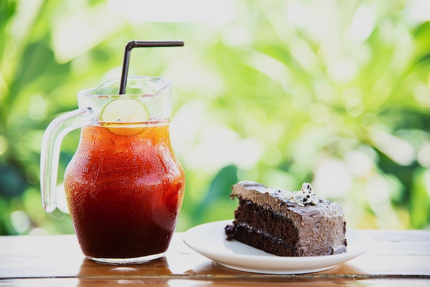 Schokoladenkuchen auf Tabelle mit Eistee über grünem Garten - entspannen Sie sich mit Getränk und Bäckerei im Naturkonzept