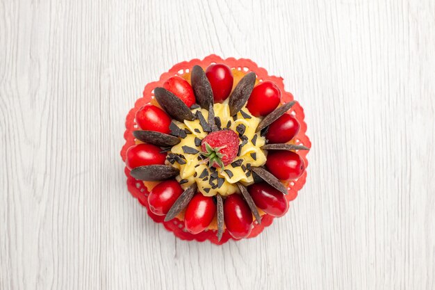 Schokoladenkuchen der oberen Nahansicht mit Beeren auf dem roten ovalen Spitzendeckchen auf dem weißen Holztisch