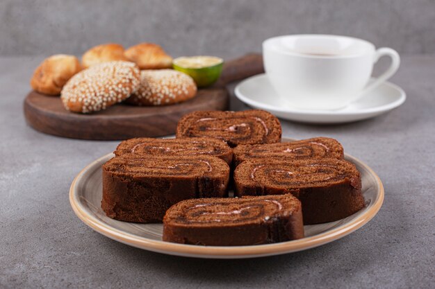Schokoladenkuchenrolle auf Keramikplatte mit schwarzem Tee
