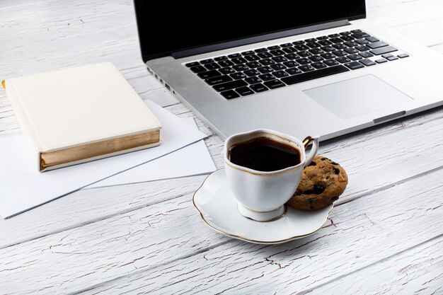 Schokoladenplätzchen liegt auf dem palte des weißen Tasse Kaffees vor einem Laptop