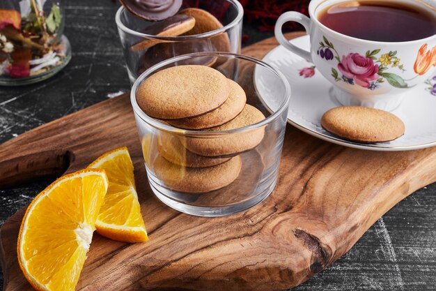 Schokoladenschwammplätzchen auf einem Holzbrett mit Orange und Tee.