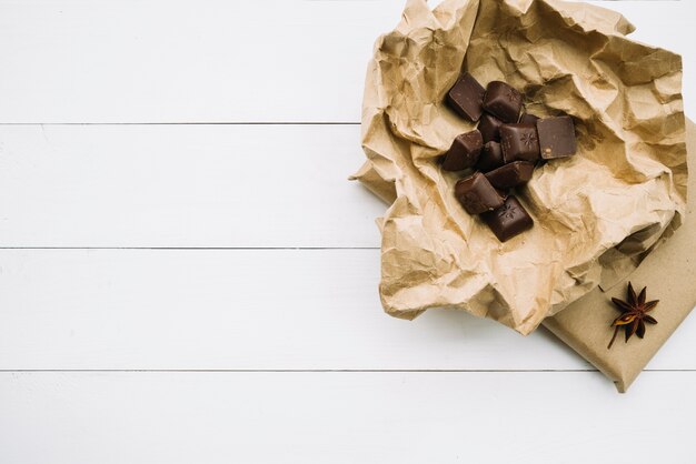 Schokoladenstücke auf zerknittertem Papier mit Sternanis auf weißem hölzernem Hintergrund
